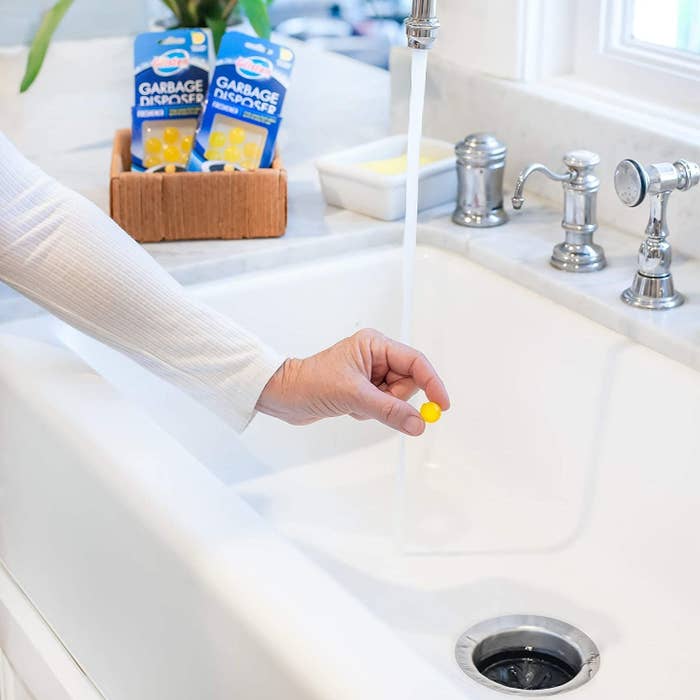 hand about to drop a small marble-sized yellow ball down the sink drain