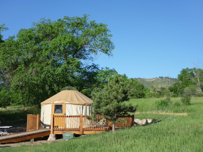 Just outside Morrison, Colorado, summer&#x27;s green colors surround the area with a small canvas covered yurt for campers in Lakewood&#x27;s Bear Creek Lake Park with the Rocky Mountains in the distance.