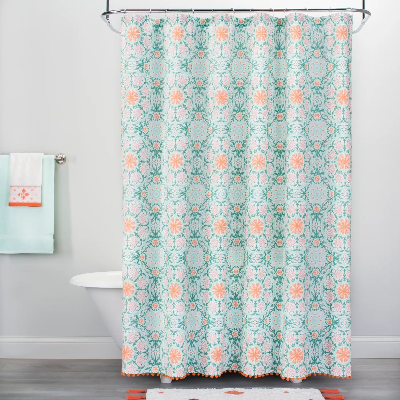 The green and orange shower curtain with a medallion print and pom poms along the bottom hanging in a shower