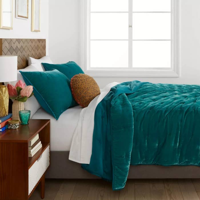 The teal velvet comforter with tufted detailing on a queen bed