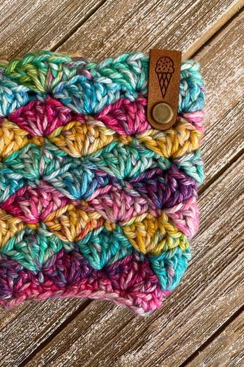 a rainbow crochet pint cozy with a leather tab featuring an engraving of an ice cream cone 