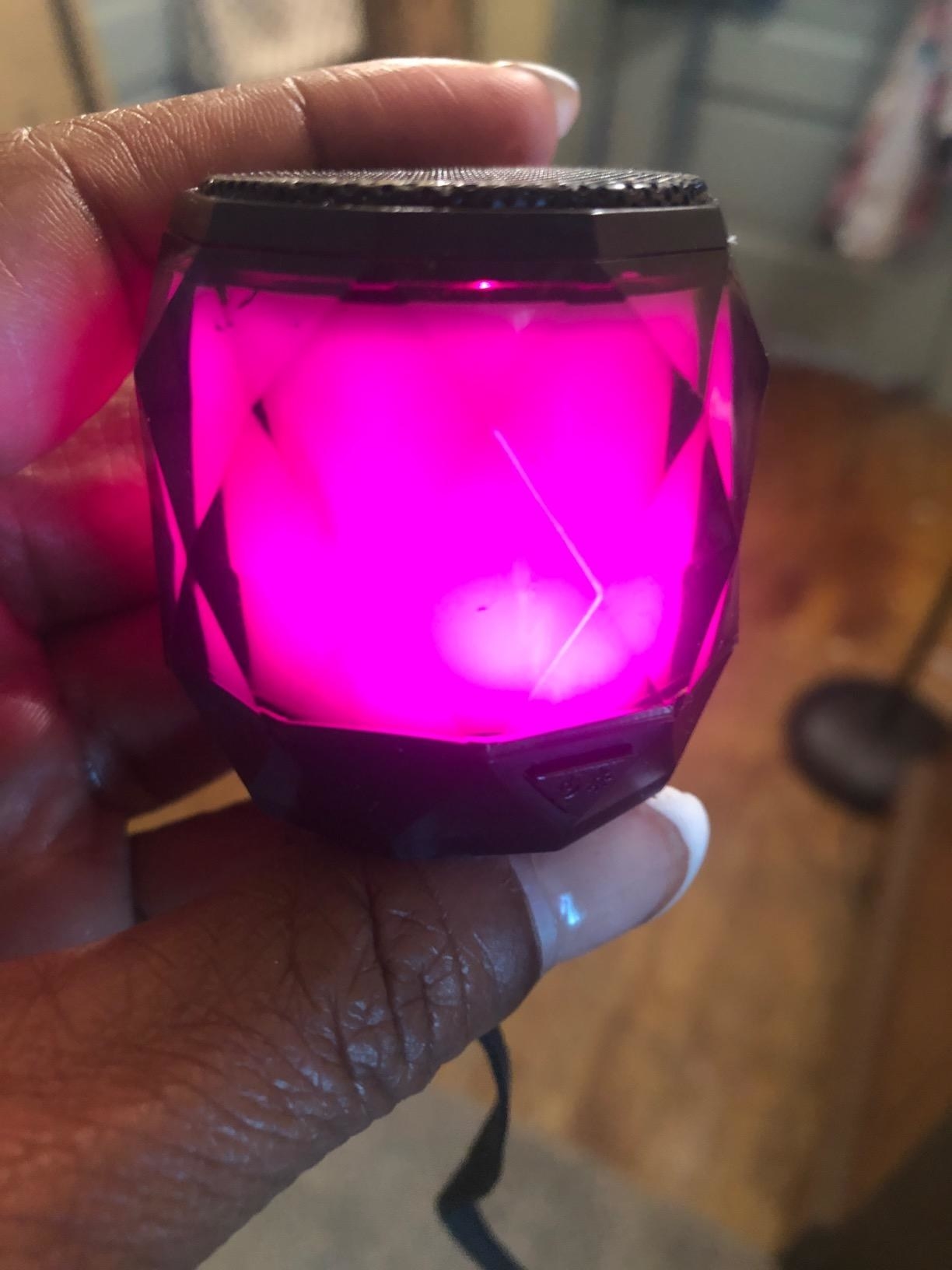 close up of reviewer holding up the portable speaker with lights turned neon fuschia