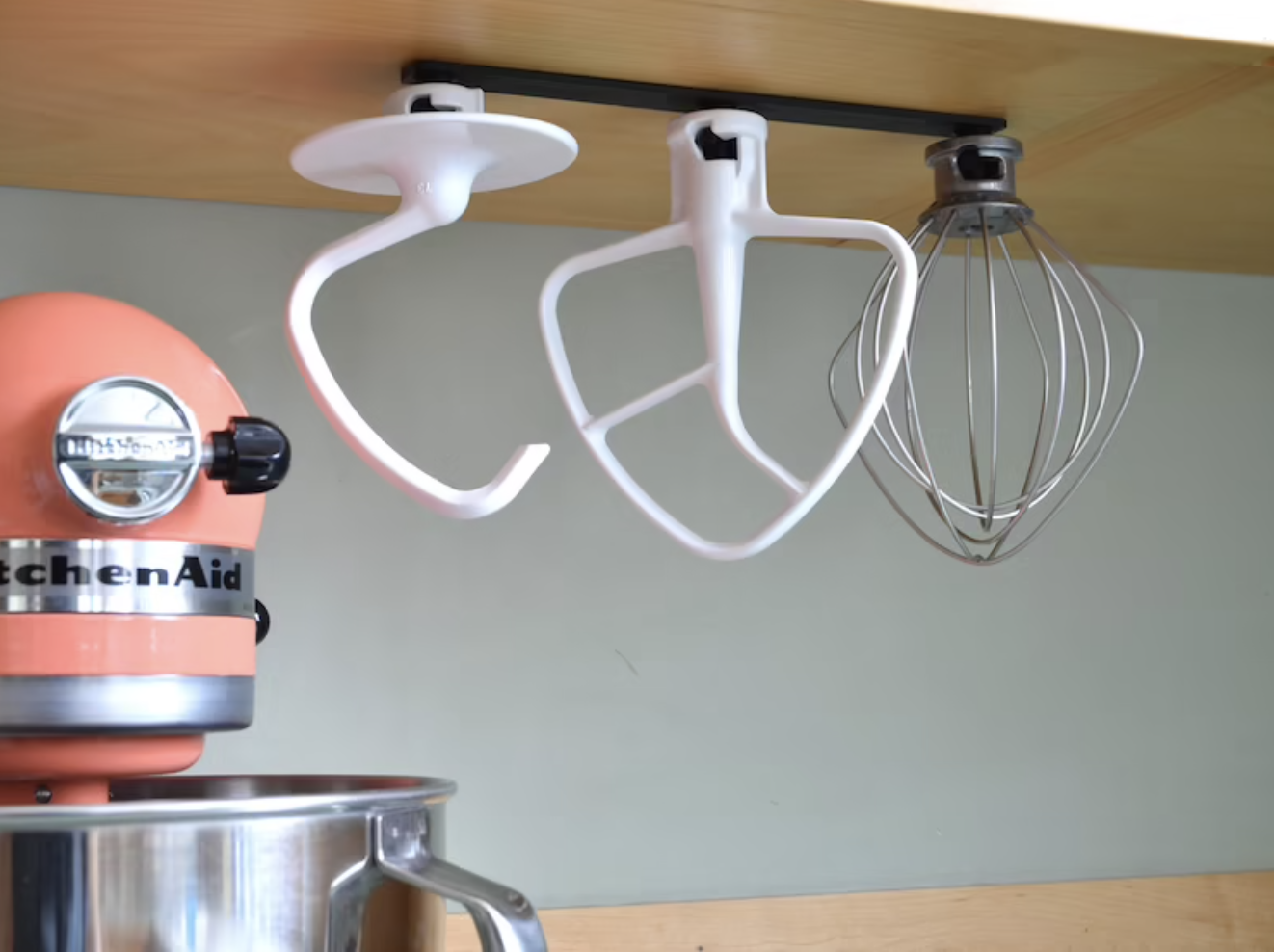 Three kitchenaid attachments hanging upside down from a cabinet from a thin black mount