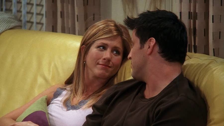 Rachel and Joey sit close together on a couch and smile at each other