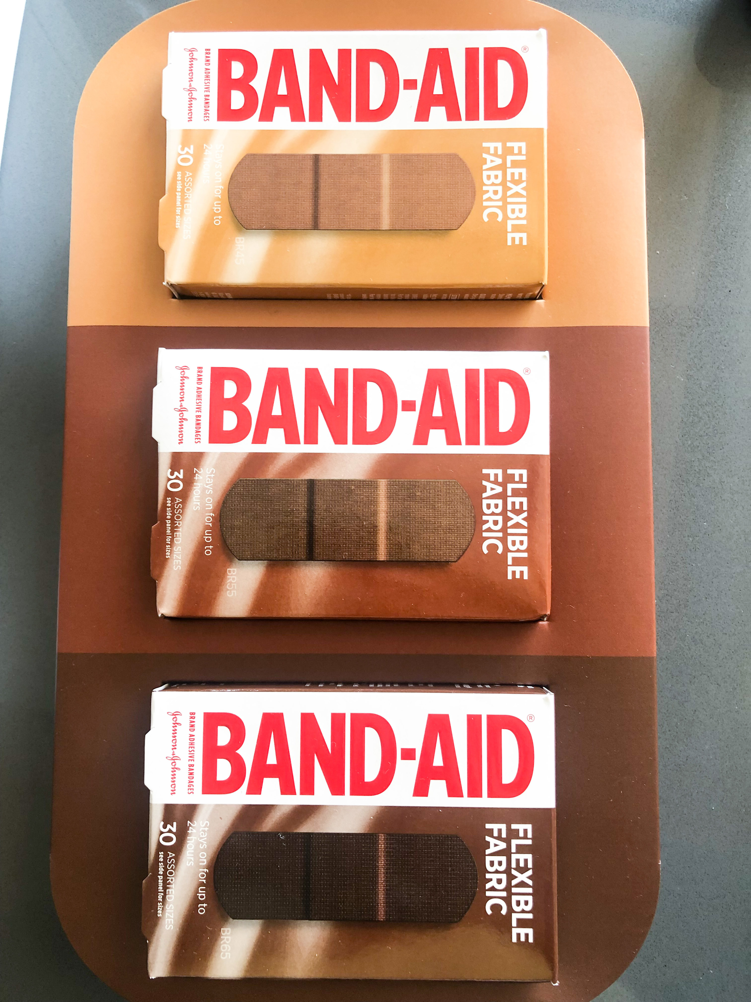 A flatlay of three boxes of bandaids in dark skin tone shades