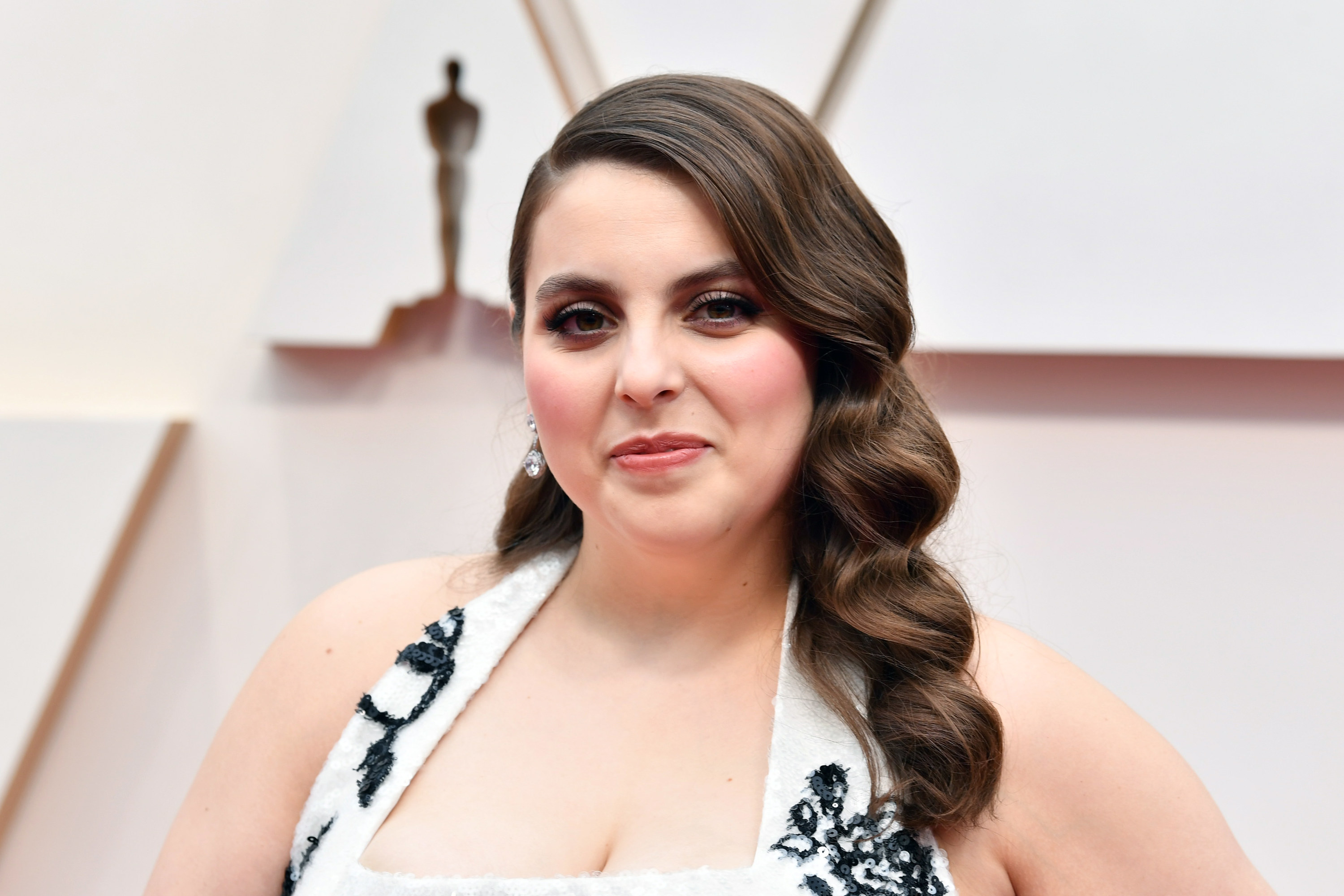Closeup of Beanie Feldstein in a white and black gown smiling at the camera