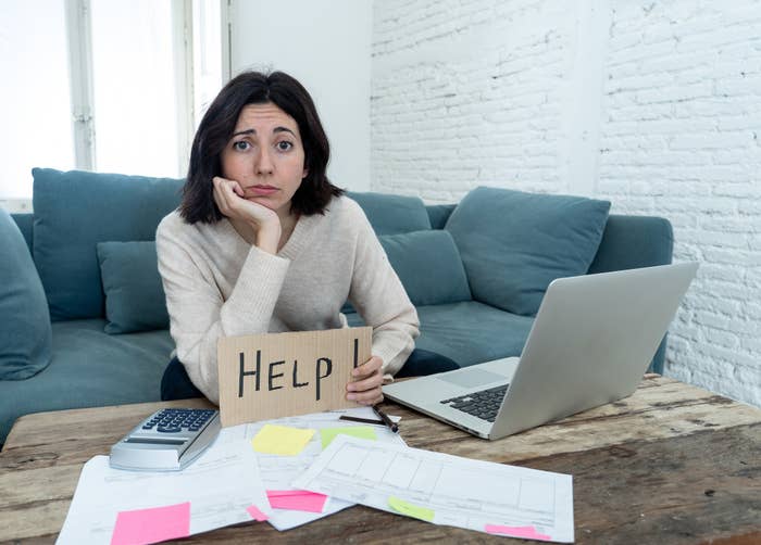 Woman looking at her bills holding a sign that says help
