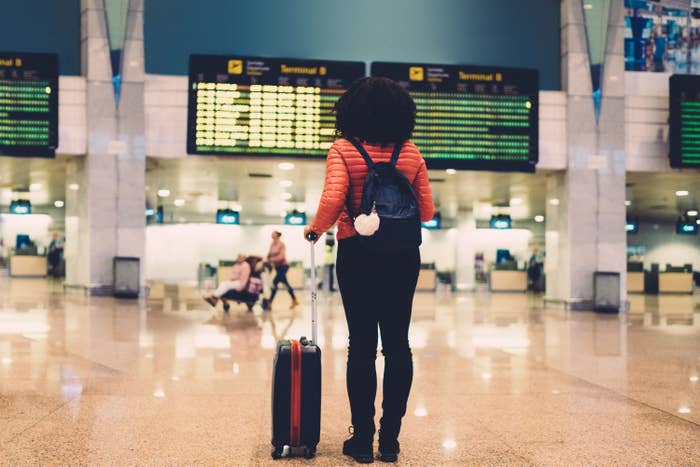 Woman looks at departure screens with her suitcase