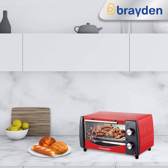 An oven toaster griller kept on kitchen slab with chicken inside and baked bread on the counter