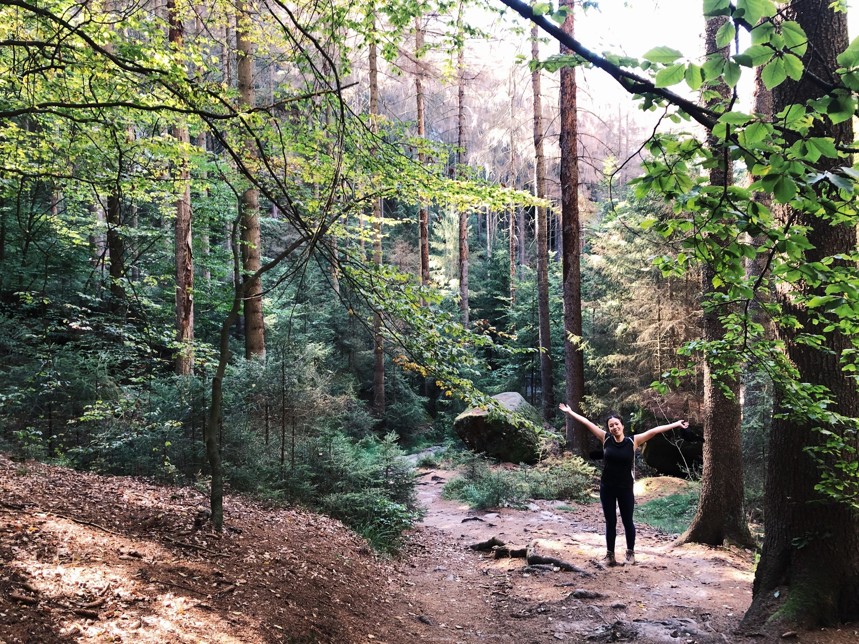 The writer holding her hands out in the middle of a verdant Berlin forest