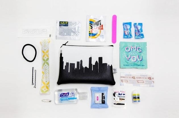 A small white faux leather pouch with a black skyline print surrounded by a mix of travel-sized toiletries and on-the-go essentials