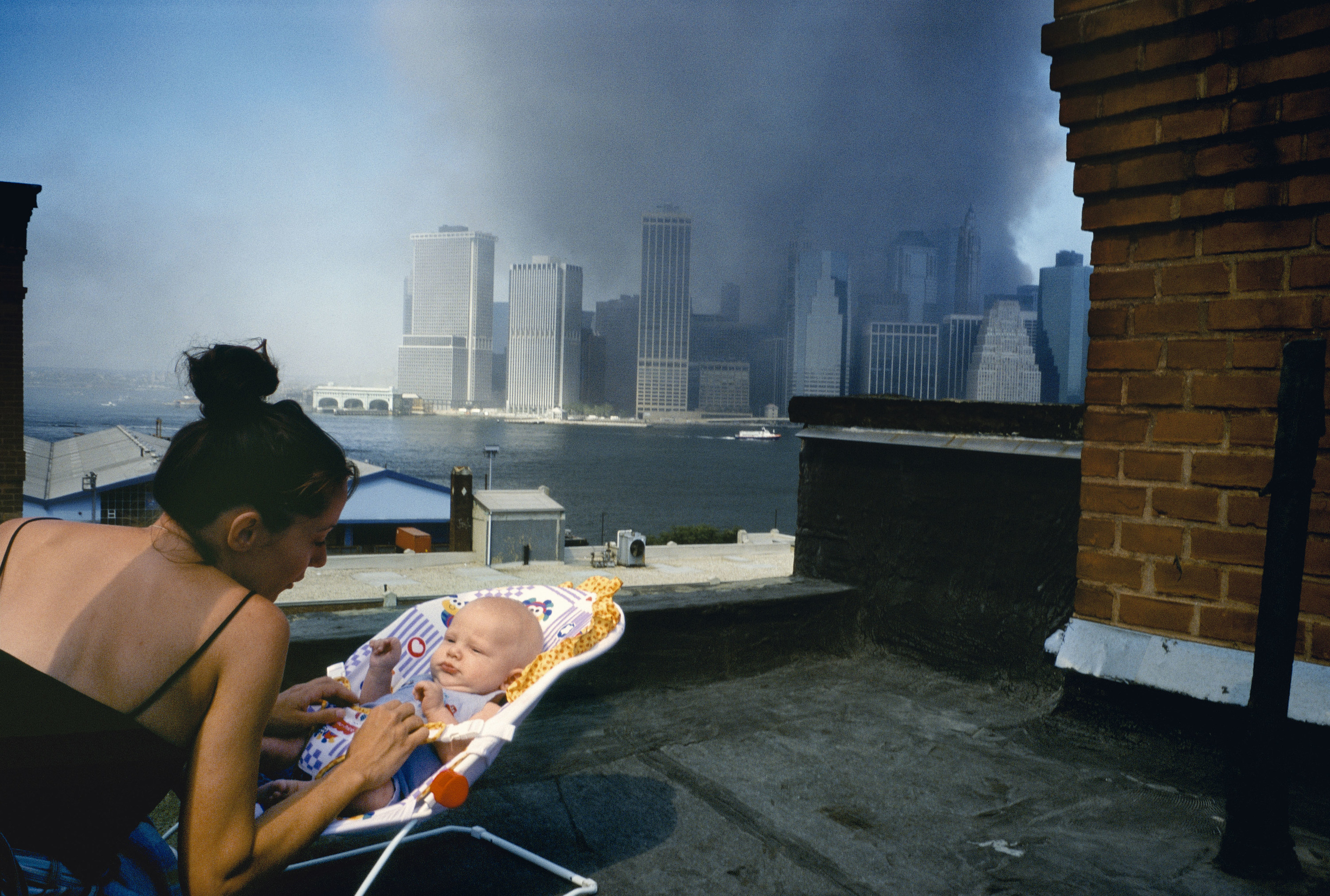 A woman with a baby on the roof overlooking the New York skyline, which is obscured with smoke from the towers