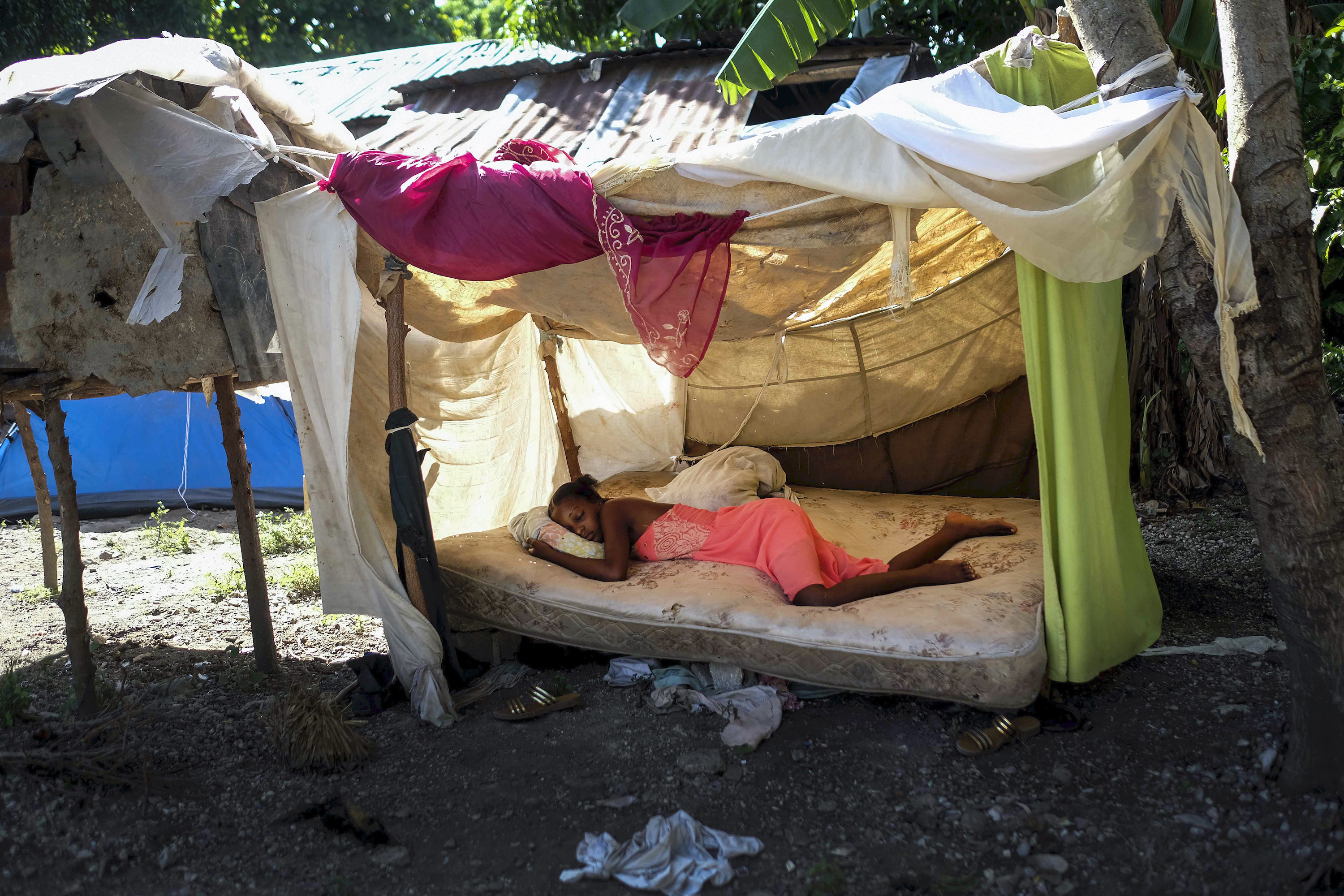 A woman sleeps under a makeshift bed on the ground under the shade of hung-up blankets
