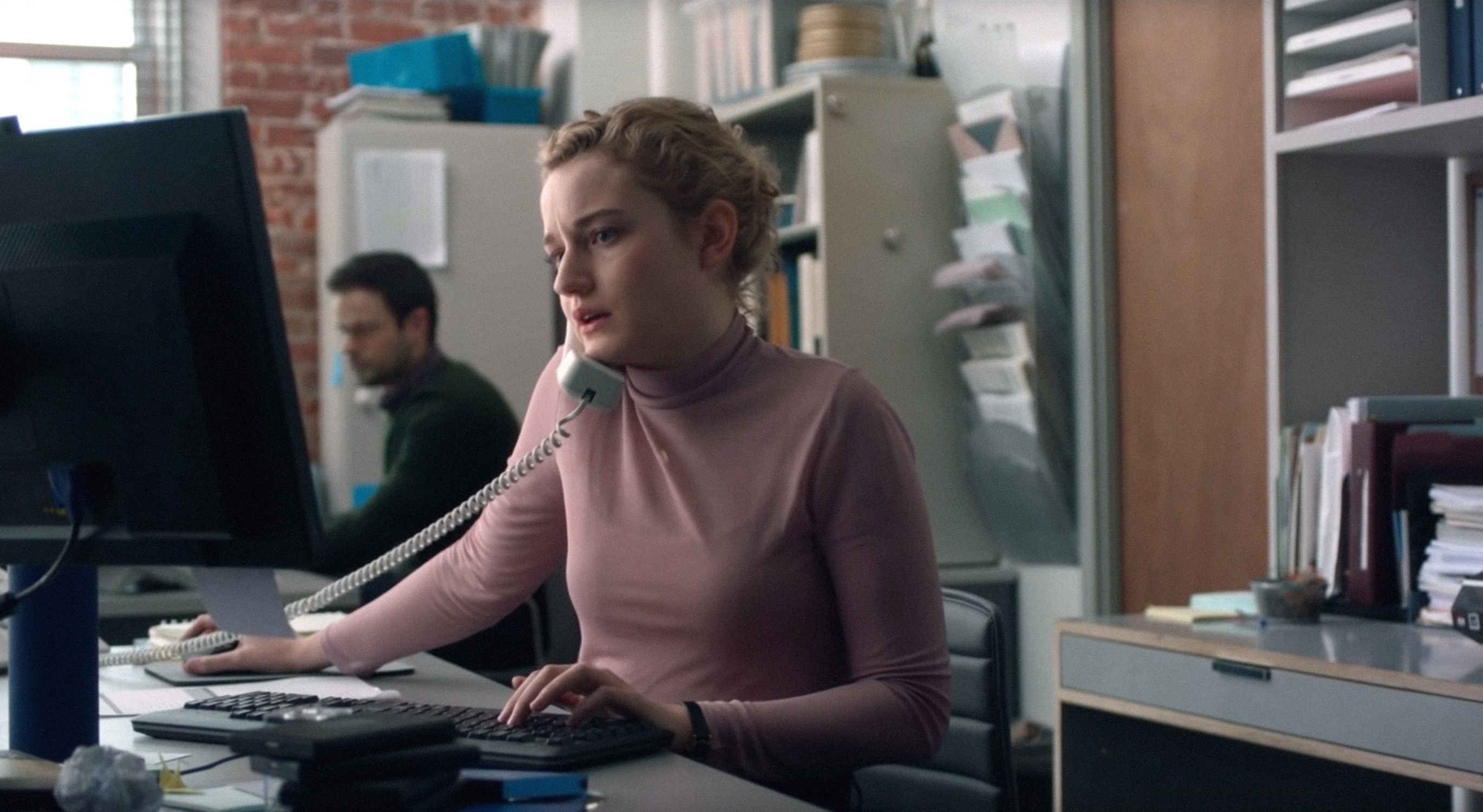 Julia Garner talking on the phone while looking at the computer at her desk