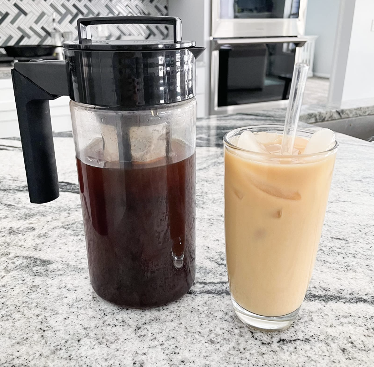 The cold brew coffee pitcher next to a cup of cold brew