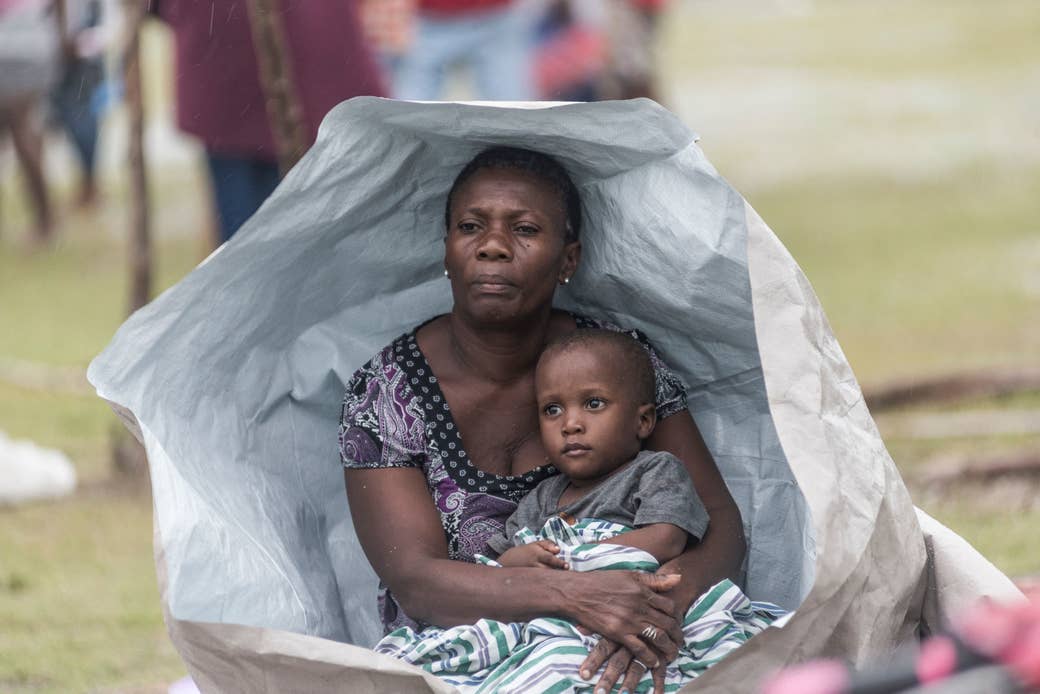 A woman holds her child as both sit under a plastic sheet