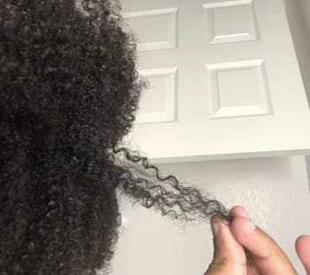Reviewer with curly hair holding a strand of it out