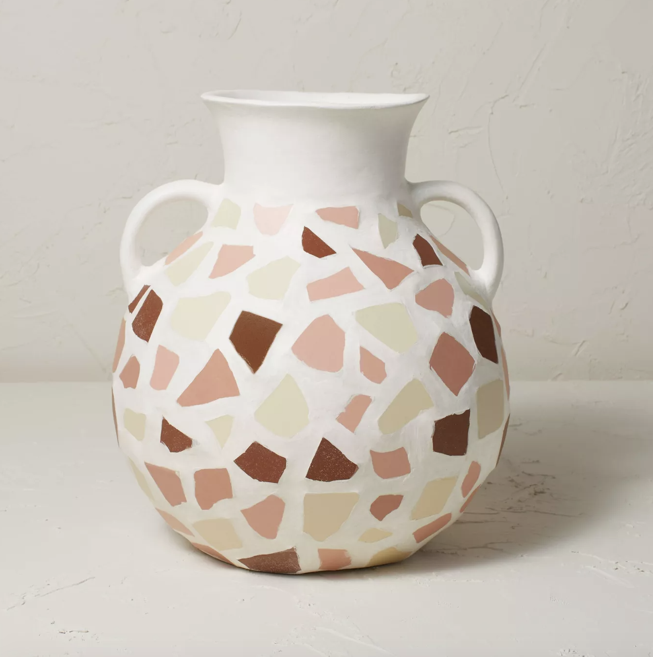 a white jug-shaped vase with pink, cream, and brown shapes on it