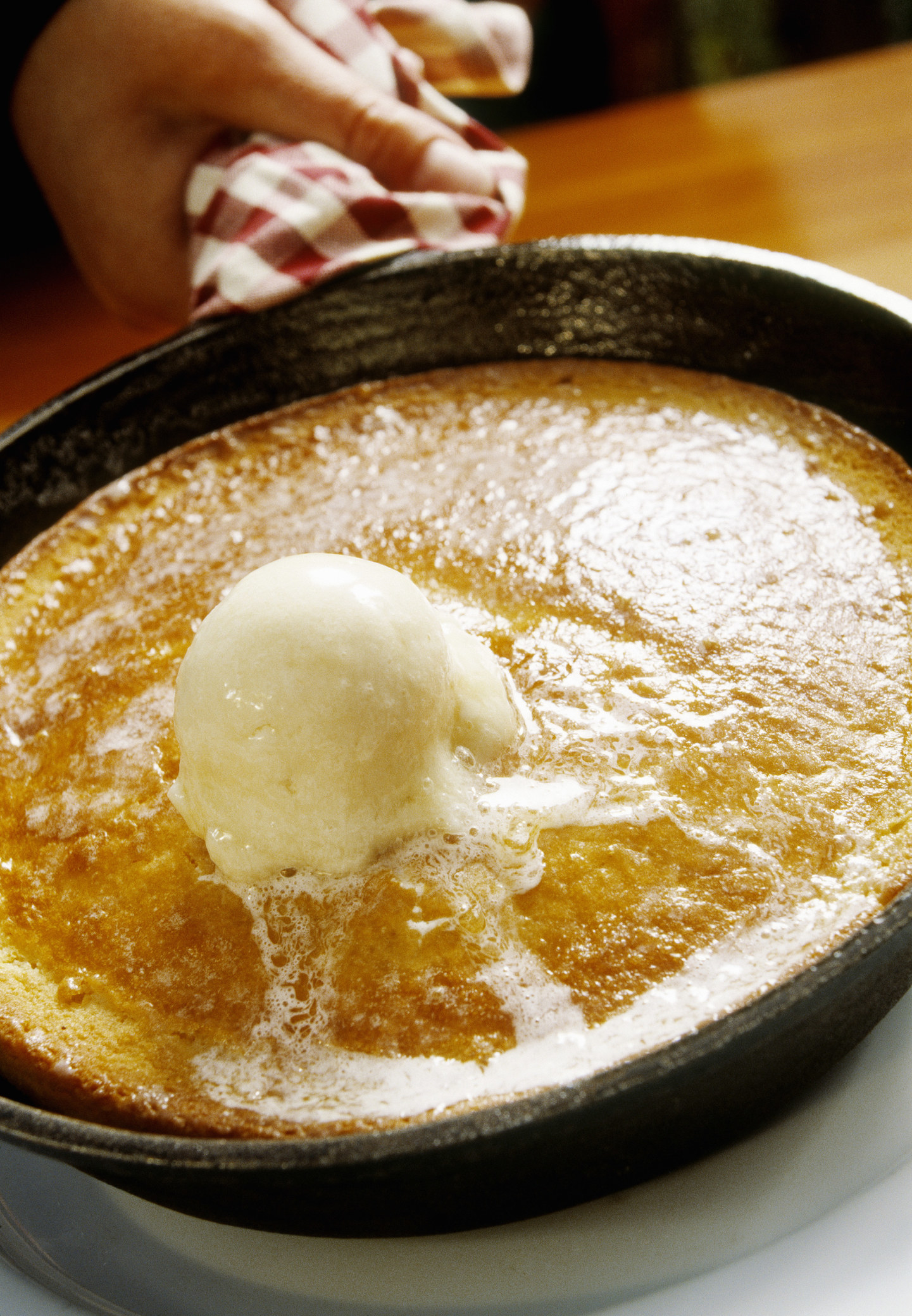 A pancake in a skillet topped with a big chunk of butter.