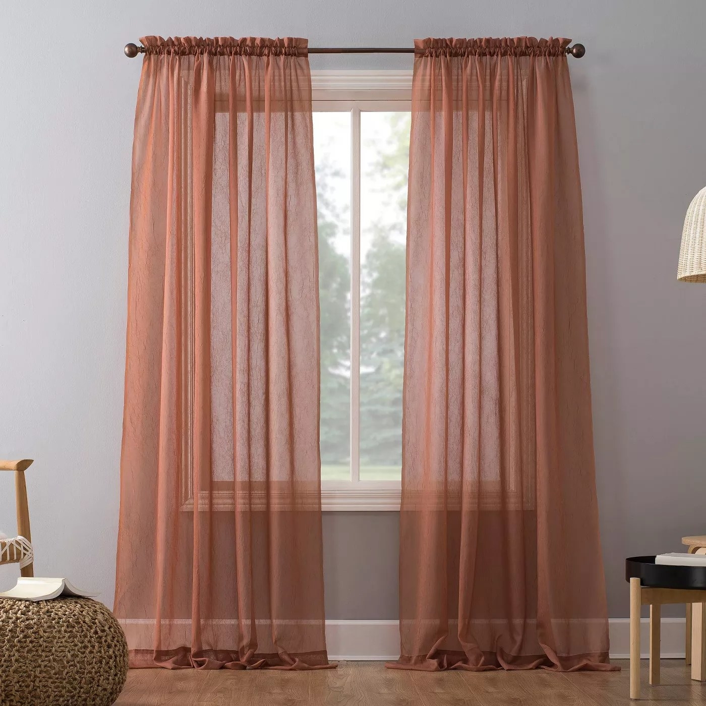 The sheer curtains are in a blush orange color and hung in a lit and cool-toned room