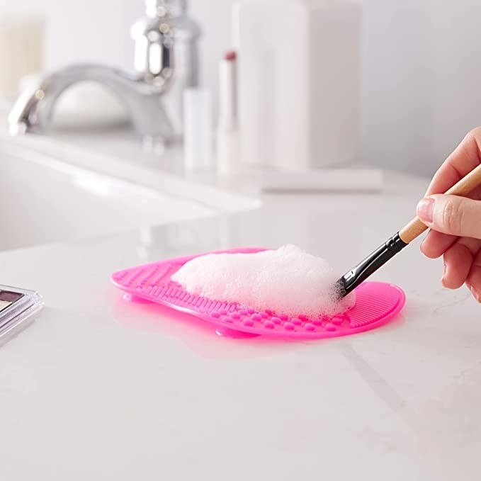 A person using the brush cleaning pad to clean a narrow brush