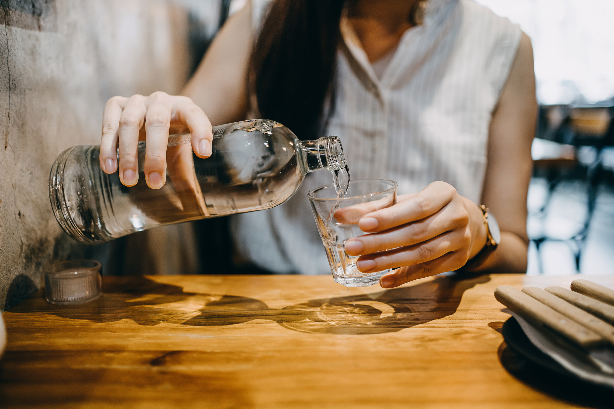 A woman pouring a pitcher of water into her glass.