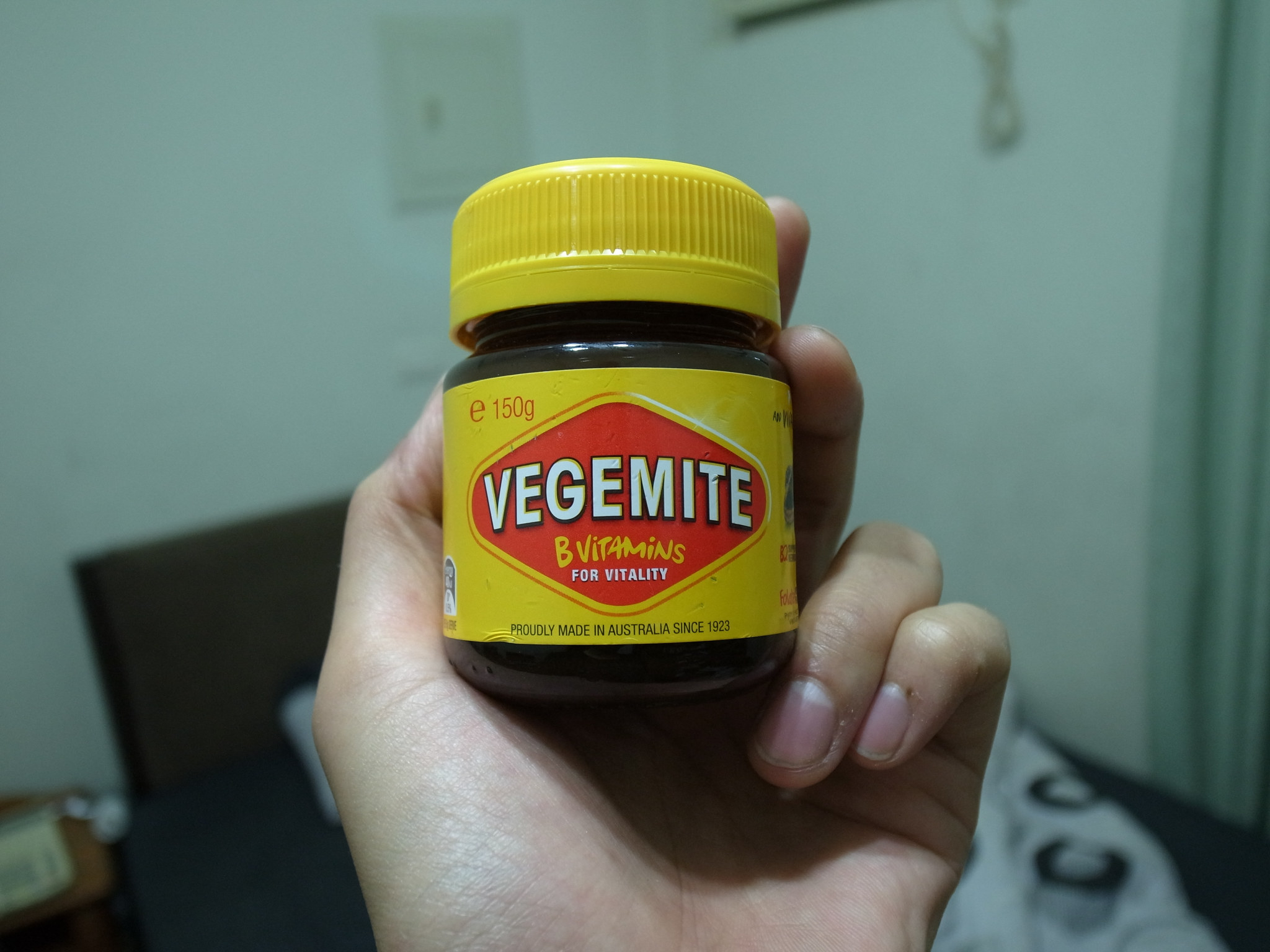 A hand holding a jar of Vegemite