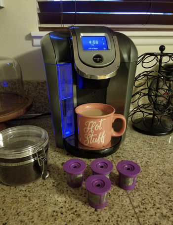 A reviewer's four purple K-cups in front of a Keurig