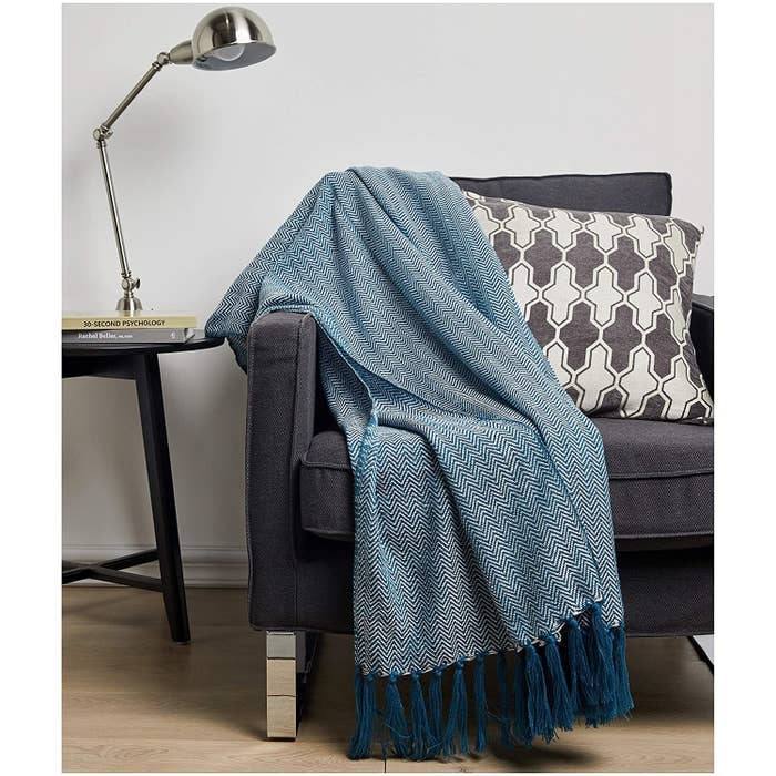 A knitted blanket with fringed edges, draped on a couch