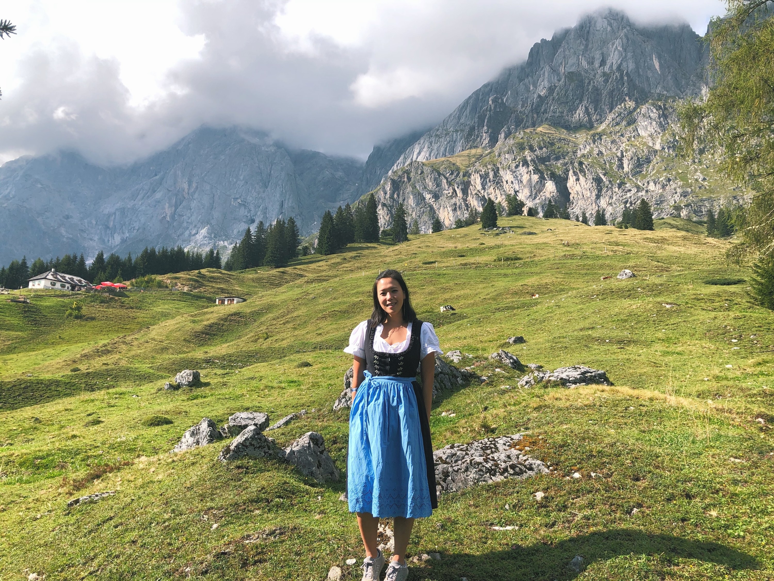 The writer wearing a traditional dirndl, standing in front of a lush mountain top