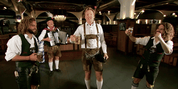 Conan O&#x27;Brien raising a traditional Bavarian beer glass while three Germans around him grin and raise their glasses in unison