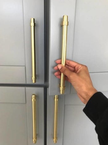 reviewer pulling gold pull on kitchen cabinet