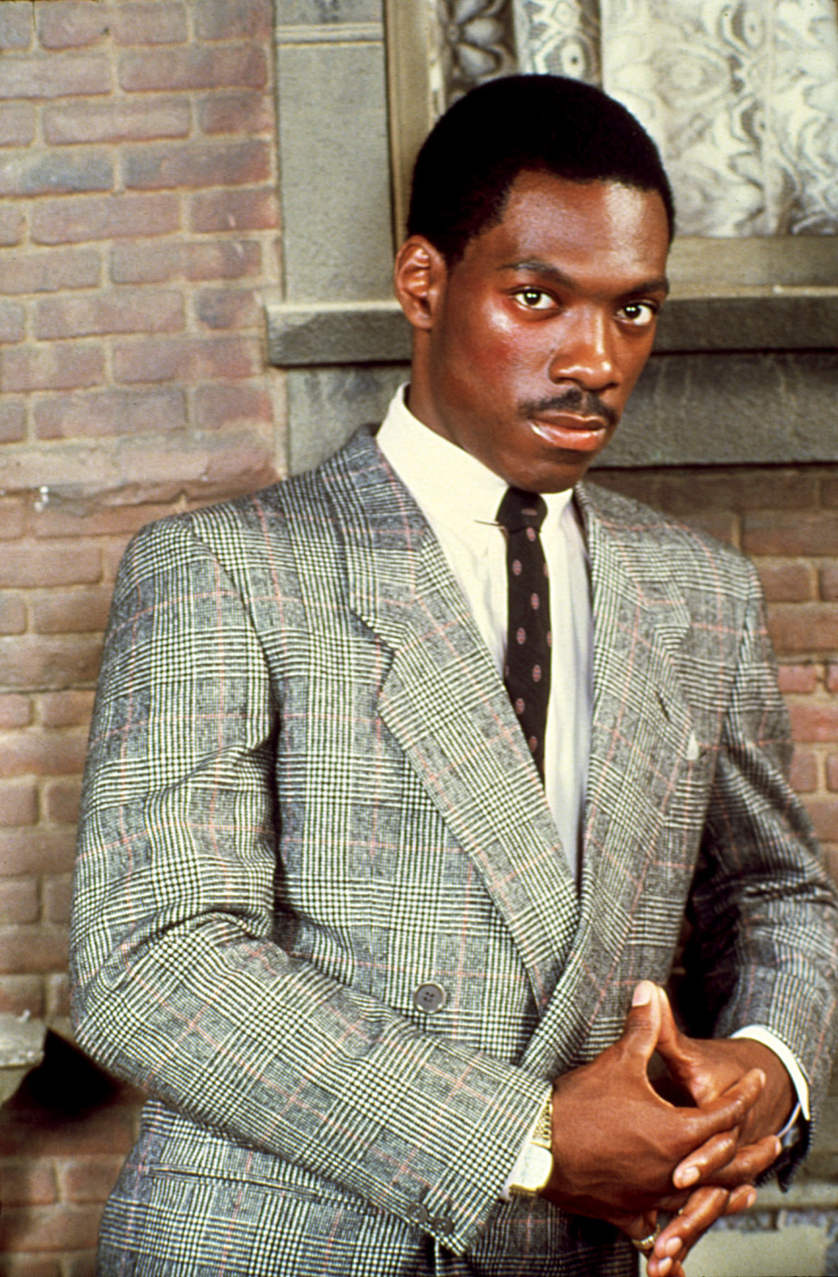 Eddie Murphy in a suit, leaning against a brick wall