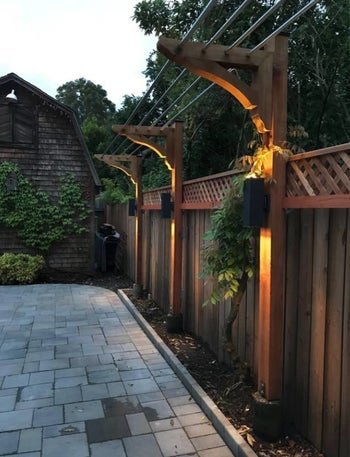 black rectangular outdoor sconce on fence above stone patio