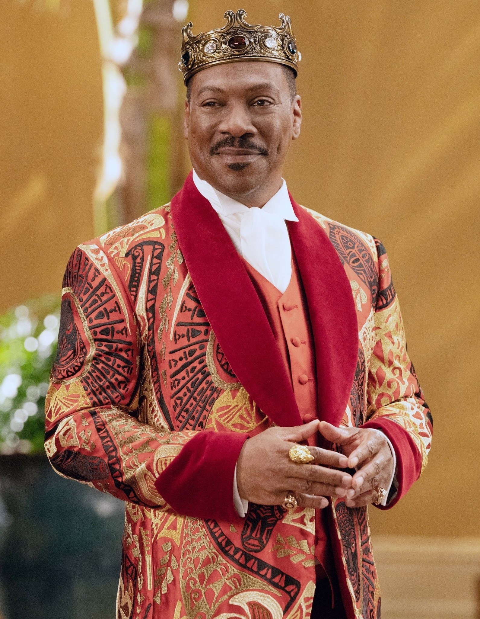 Eddie Murphy wearing a colorful blazer, a crown, and rings