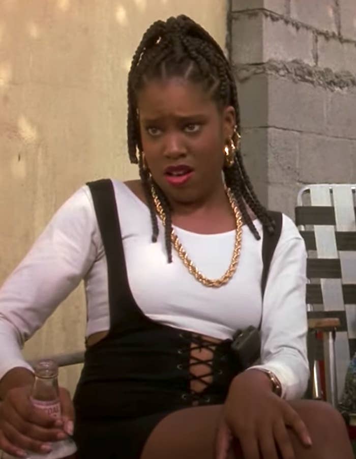 Regina King sitting down in a lawn chair, wearing a thick chain, making a confused look