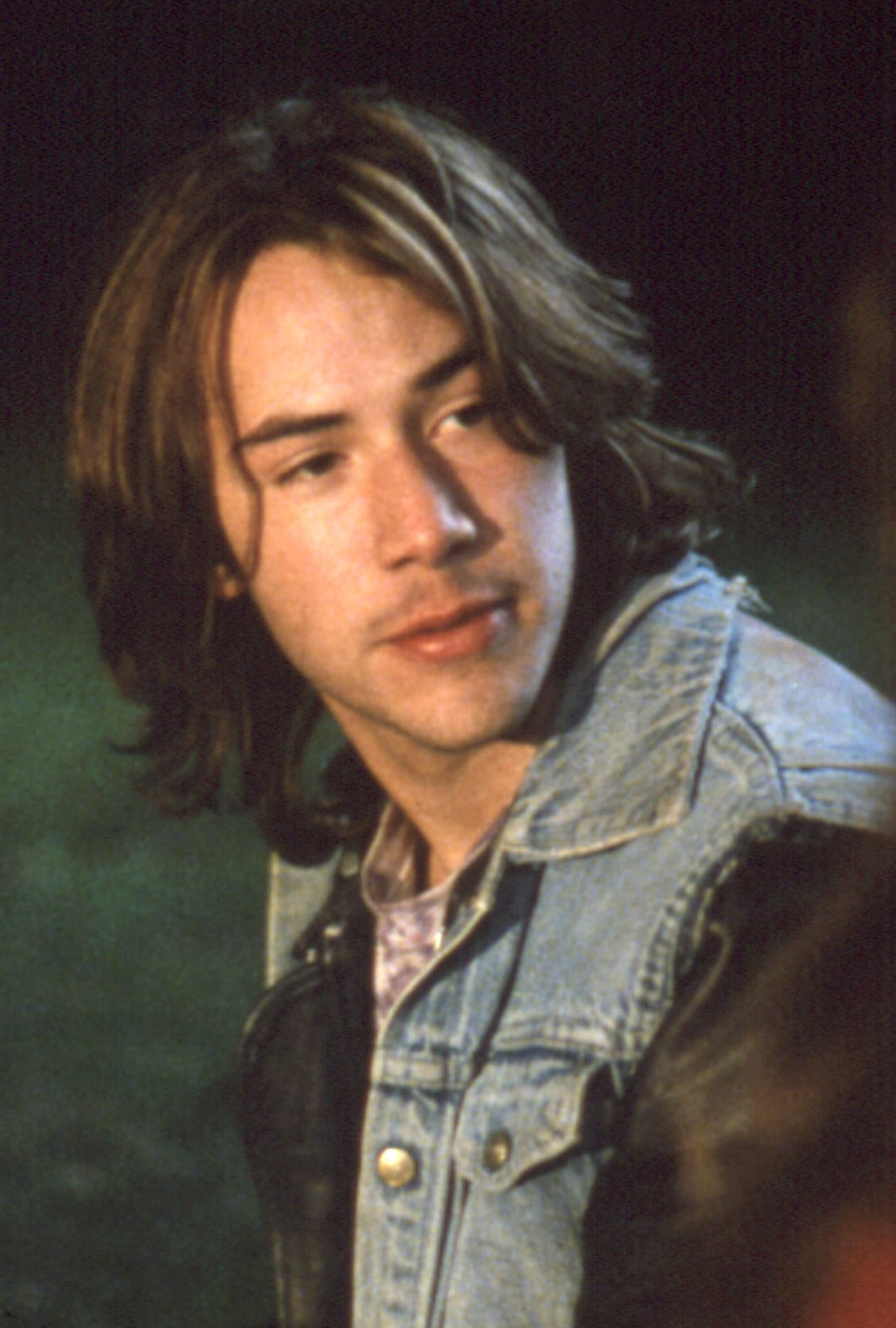 Keanu Reeves wearing a jean/leather jacket, sitting in a field