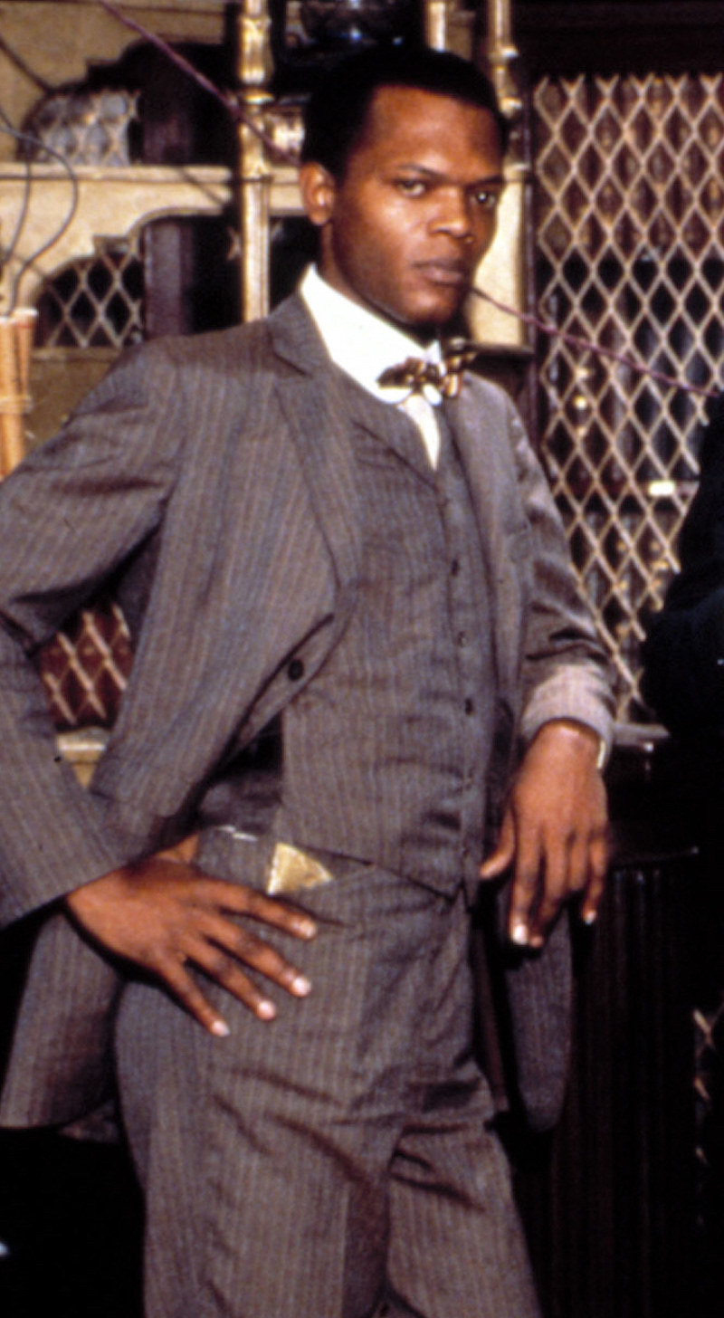 Samuel L. Jackson wearing a matching three-piece suit, leaning against a fence with his hand on his hip