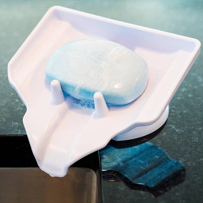 A white tilted soap holder with two hooks to keep the blue soap from falling, while also draining the soap residue