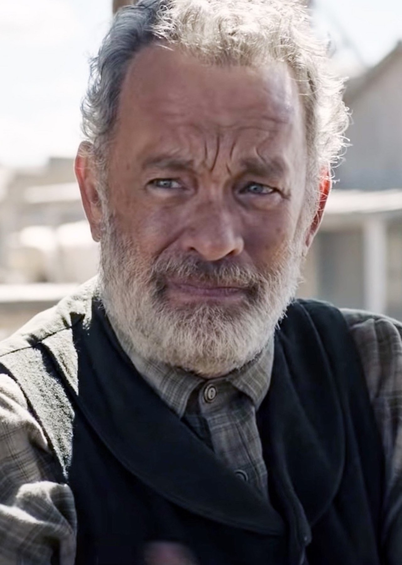 Tom Hanks with a grey beard, wearing a flannel shirt and sweater vest