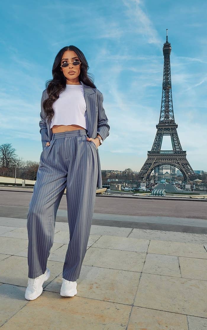 Model wearing grey striped pant, sneakers, graphic tee and blazer