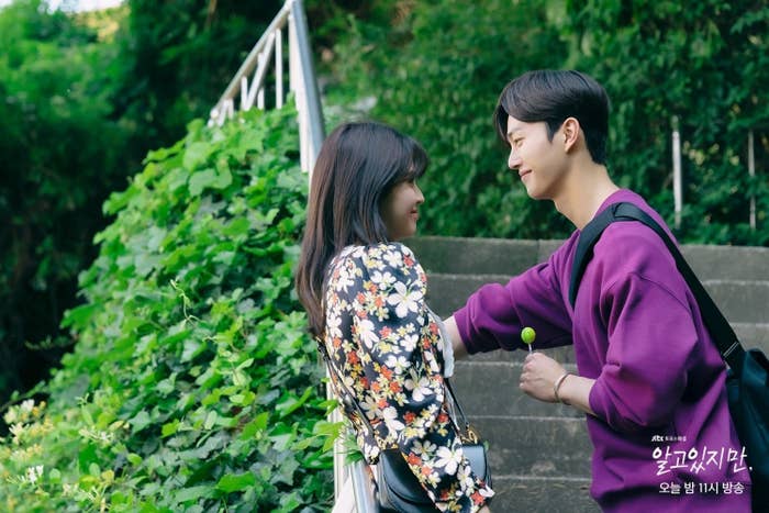 Na-bi leaning back on handrail outside with Jae-eon with one hand on handrail and one hand holding a lollipop