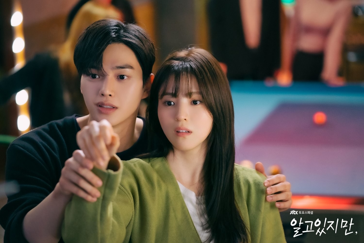 Jae-eon behind Na-bi at a bar helping her aim dart