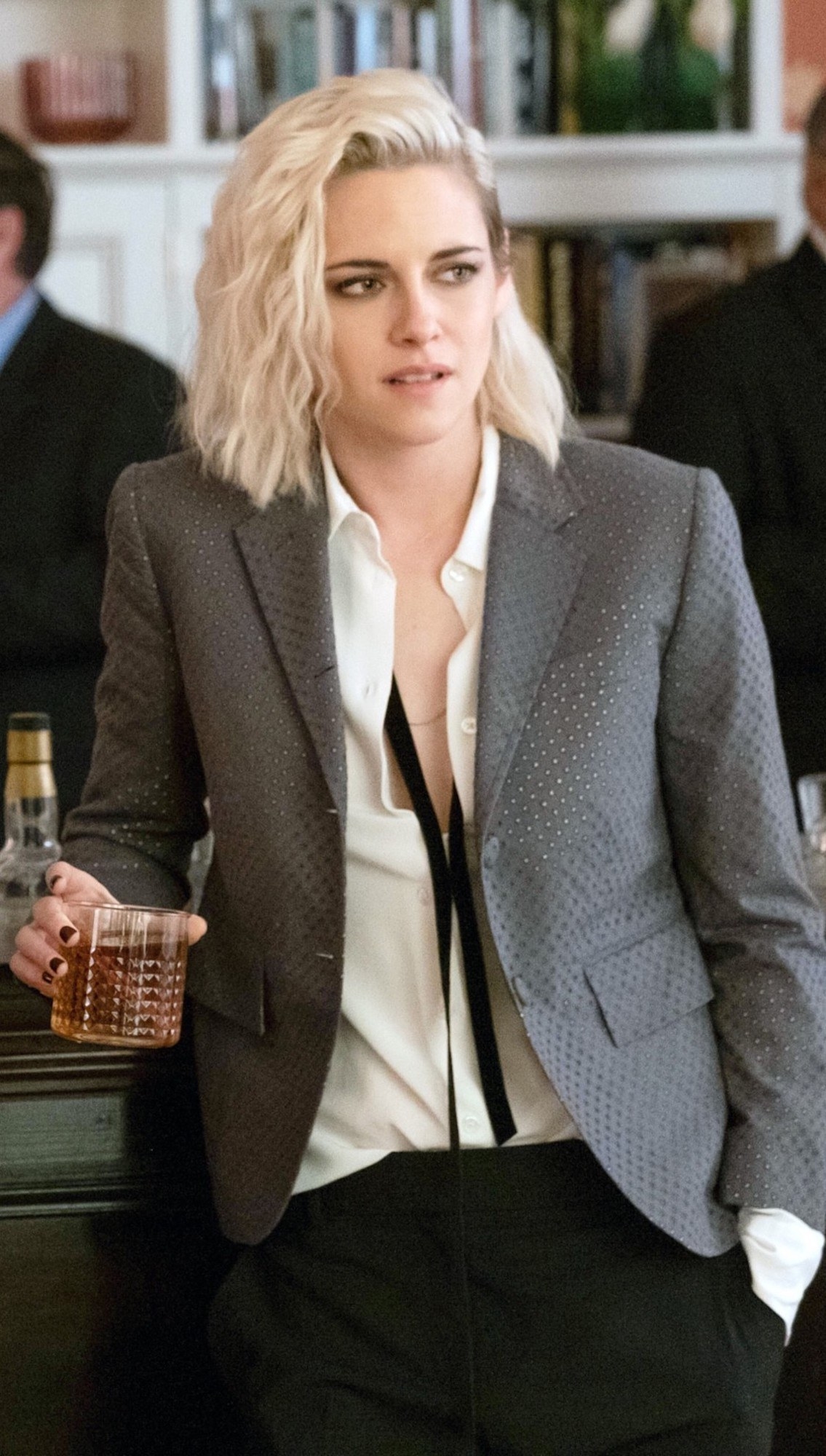 Kristen Stewart leaning up against a bar while holding a cocktail