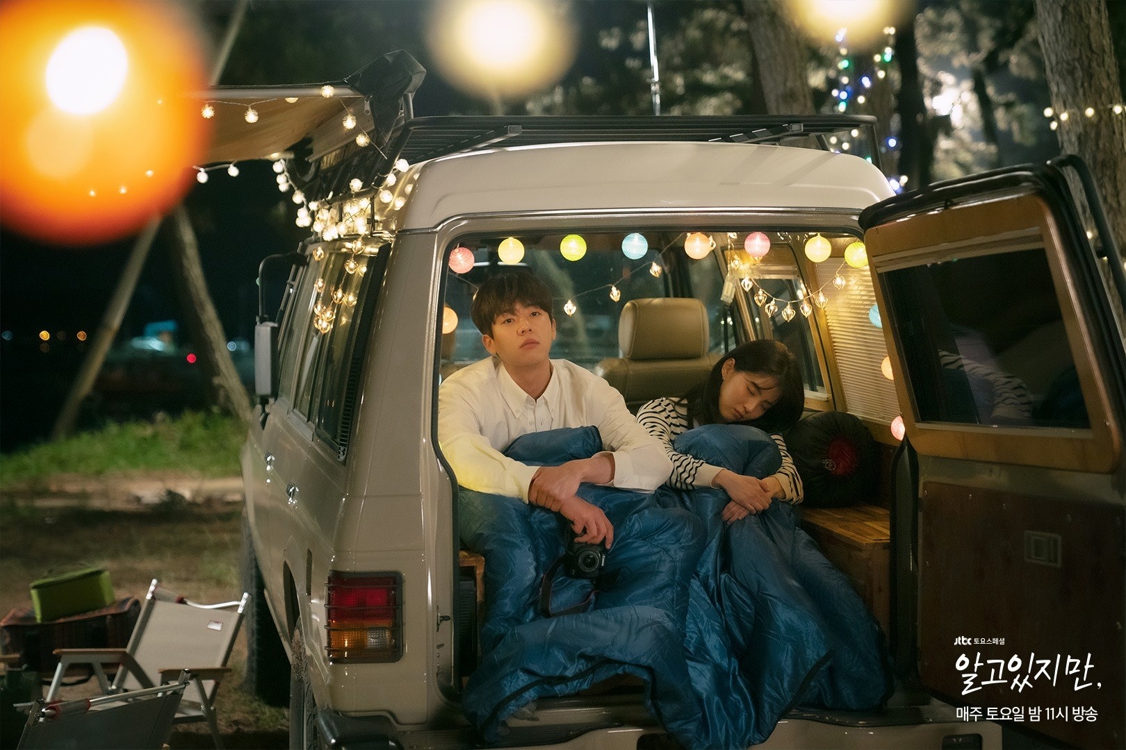 Do-hyeok and Na-bi in the back of a van at night covered in a blanket. Do-hyeok is leaning forward with a camera in his hands while Na-bi is asleep next to him