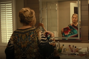 Tanya looking in the bathroom mirror holding up a dress