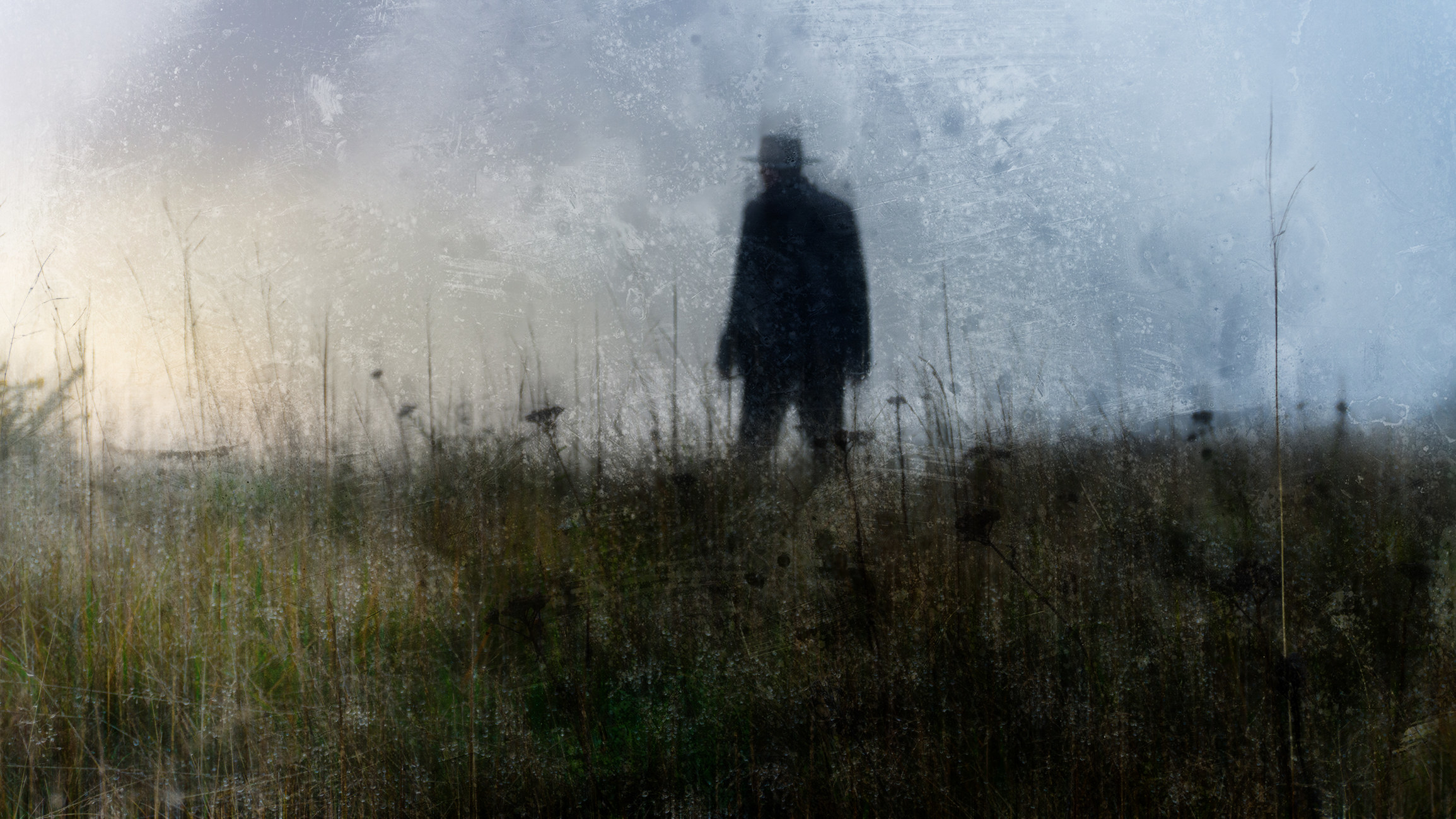 Silhouette of a man with a wide-brimmed hat walking in the tall grass