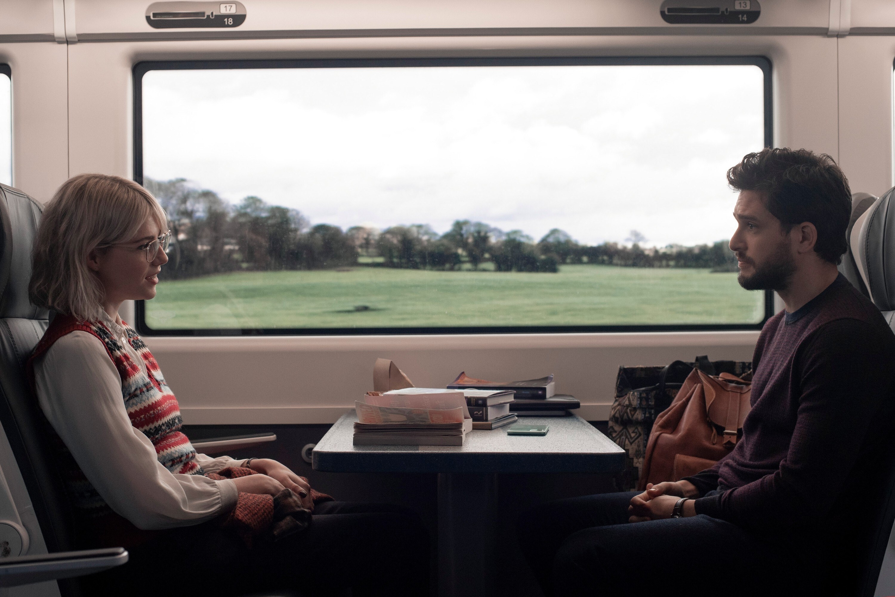 A girl and guy facing each other with a table between them on a train