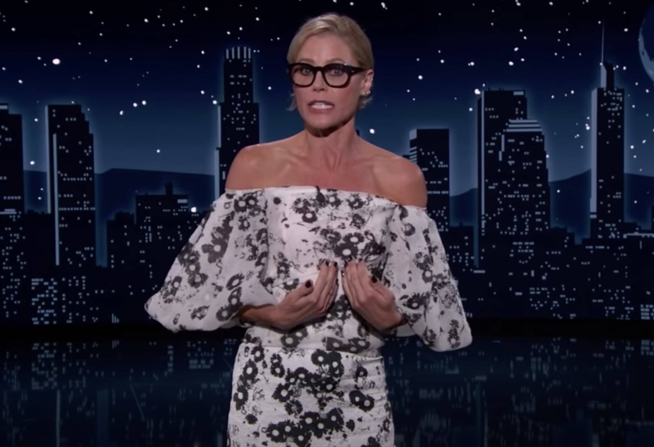 Julie wearing dark-framed glasses and an off-the-shoulder outfit as guest host of Jimmy Kimmel Live