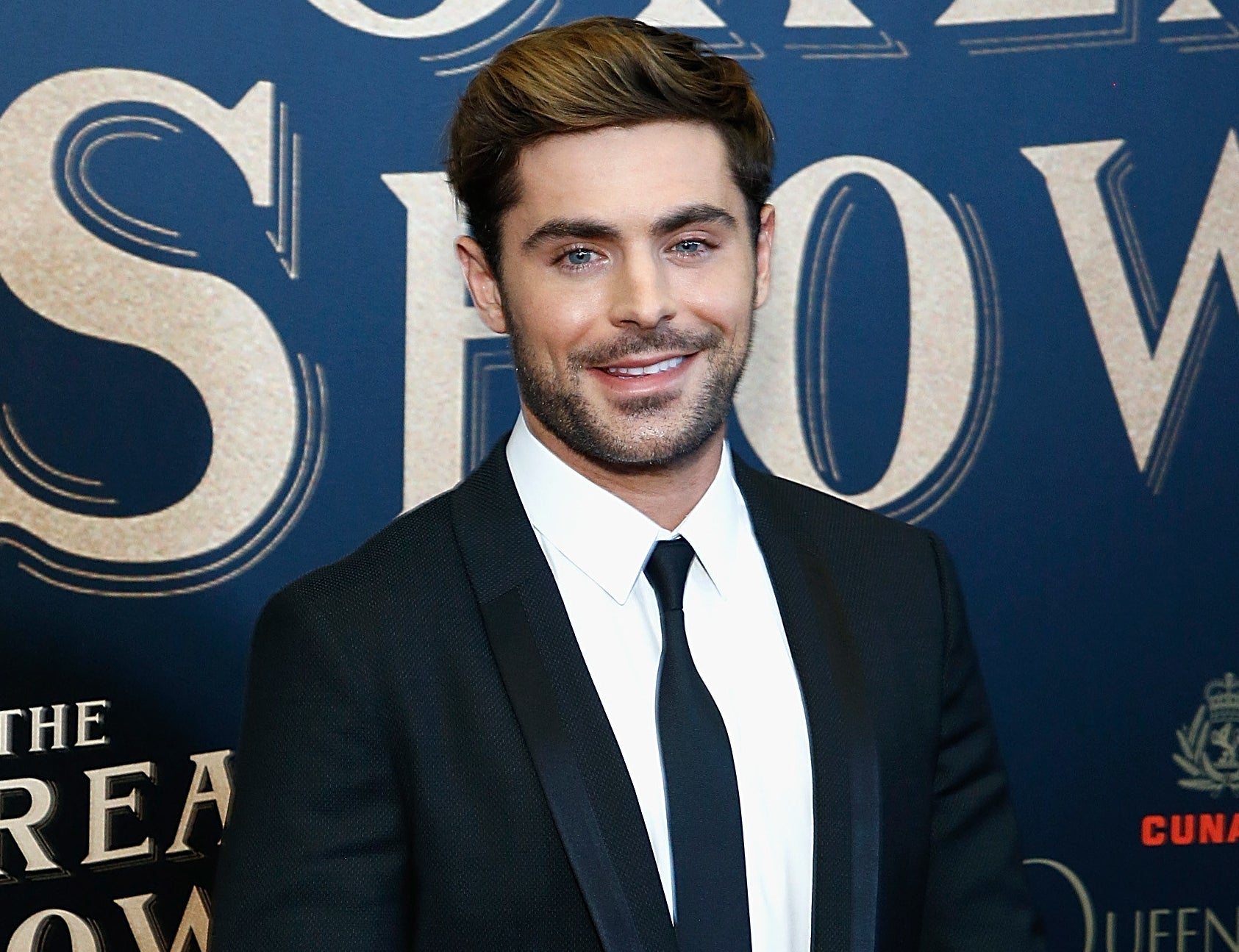 Zac smiles while wearing a suit on a red carpet